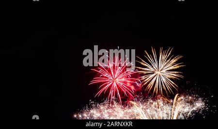 Red starburst firework, gold starburst firework over multiple gold sparkling streamers photographed against a black sky on the Fourth of July in MN Stock Photo