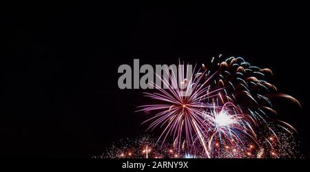 White starburst firework with multiple small gold bursts and red highlights photographed against a black sky on the Fourth of July in Minnesota Stock Photo