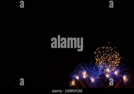 Blue starburst fireworks with white centers and small gold bursts photographed against a black sky on the Fourth of July in Minnesota Stock Photo