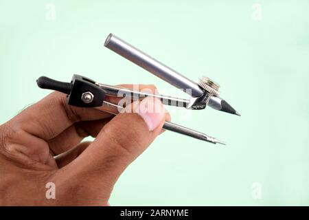 a person holding a silver pencil compass while it is attached to a silver pencil. Stock Photo
