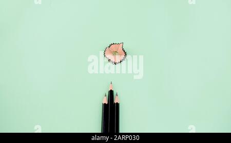 three sharp black pencil pointing toward some pencil peels which is lying on a light green background. Stock Photo
