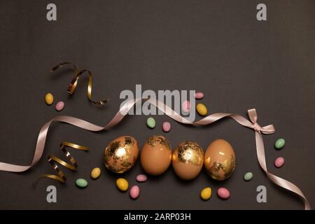 Happy easter concept. Golden eggs, color candy on a dark background, Layout or template for banner, article, product advertisement. Stock Photo