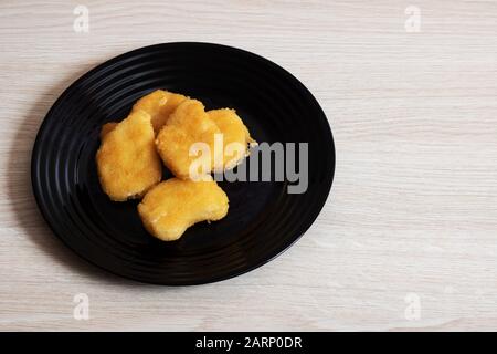 Chicken nuggets on a black plate on a birch table Stock Photo