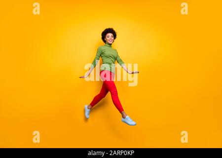 Full length body size turned photo of curly wavy brunette hair girl running jumping in red trousers white footwear isolated vivid color background Stock Photo