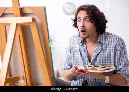 The young handsome man enjoying painting at home Stock Photo