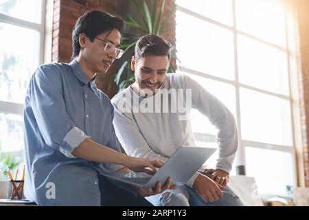 Two men colleagues sharing creative ideas, using digital tablet Stock Photo