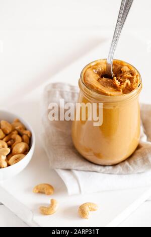 Homemade natural paleo nut peanut cashew creamy butter in glass jar and spoon on white background.Vertical orientation Stock Photo
