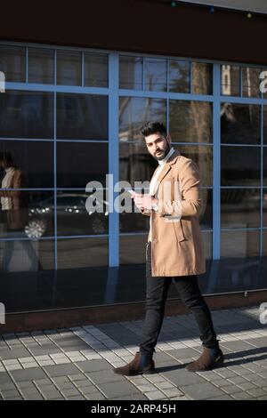 Young Indian businessman using his smartphone at street while walking. Stock Photo