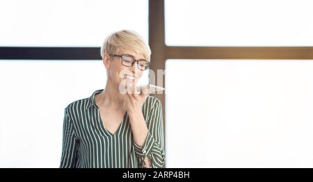Mature Businesswoman Talking On Phone Using Loudspeaker In Office, Panorama Stock Photo