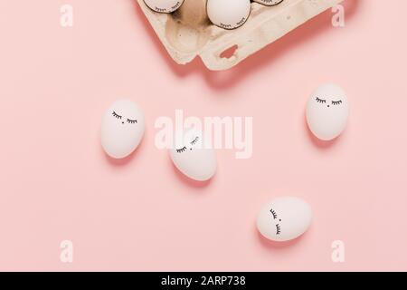 Happy Easter. White eggs with painted eyes in paper packaging on pink background. Flat lay, top view, copy space. Stock Photo
