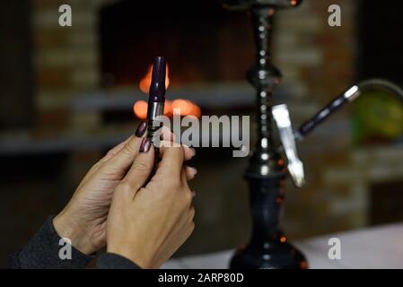 Hookah mouthpiece with a stream of smoke in a beautiful female hand on a dark background. hand and hookah pipe. Hookah in the dark at night against th Stock Photo