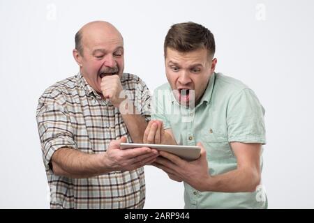 Caucasian mature father and son looking in internet for the latest news using electronic tablet. Studio shot Stock Photo