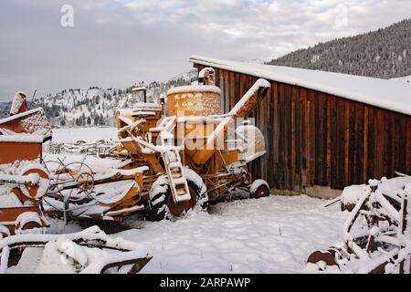 Snow-covered farm implements on the side of an old wooden barn, on a remote horse farm in Beavertail, Montana.  Beavertail is located east of Clinton, Stock Photo