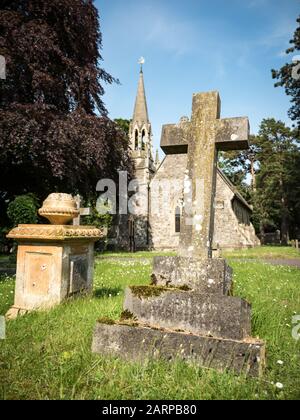 Traditional old English grave yard scene with a crucifix headstone in the foreground and a small chapel of rest behind. Stock Photo