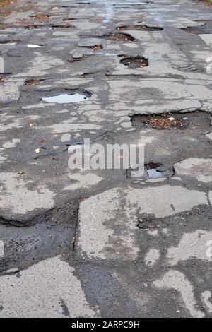 Old ruined asphalt road with potholes and bumps. Wet autumn road with leaves. Stock Photo