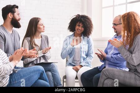 Happy afro woman appreciating support of people at rehab group meeting Stock Photo