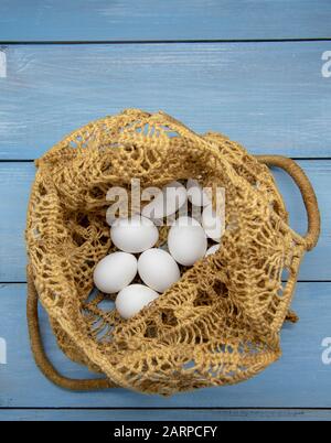 White eggs in a wicker bag on a blue wooden tabletop. Stock Photo