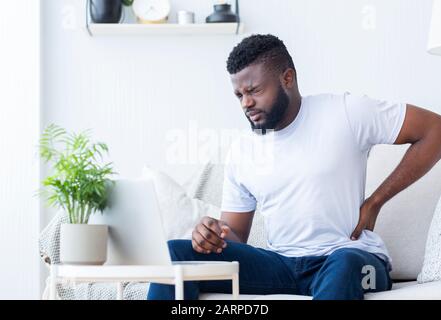Working on laptop african man suffering from back pain Stock Photo