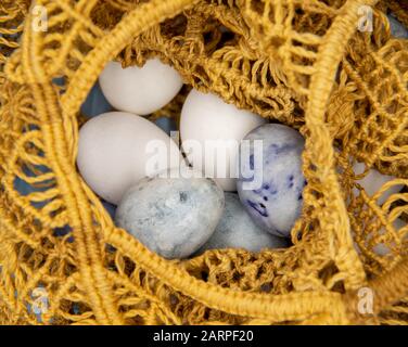 White and painted eggs in a wicker string bag . Stock Photo