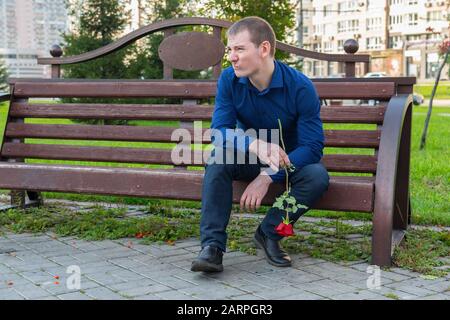 Displeased man with a rose in his hands is watching someone in the park Stock Photo