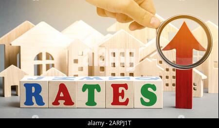 Wooden blocks with the word rates, up arrow and miniature houses. The concept of high interest rates on mortgages. Real estate. Credit. Loan Stock Photo