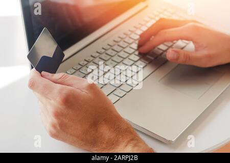Man's hands holding a plastic credit card near the laptop close-up. Online shopping or making payment. Stock Photo