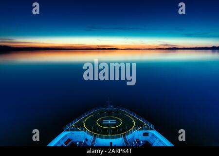 Cruise ship is facing beautiful sunset. Helipad is ready to get a helicopter at any time. Blue and calm sea is supporting navigational team. Stock Photo