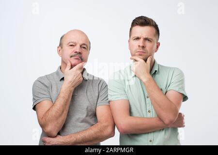 Serious two caucasian men hold chins being deep in thoughts, find way out of problem. Family problem concept. Studio shot Stock Photo