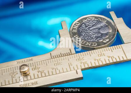 UK new pound coin between brass Vernier caliper jaws. For price inflation, value of pound sterling, investment savings performance, rising costs. Stock Photo