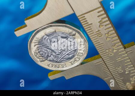UK new pound coin between brass Vernier caliper jaws. For price inflation, value of pound sterling, investment savings performance, rising costs. Stock Photo