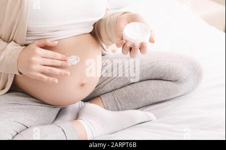 Pregnant woman applying cream on her big belly, close up Stock Photo