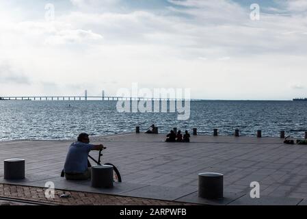 Malmö, Sweden - August 30, 2019: People sunbathing on the dike in the promenade in front of the Baltic Sea and the Öresund Bridge on summer in Västra Stock Photo