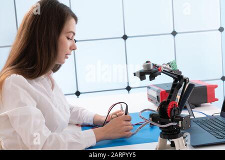 A young woman writes an algorithm for the robot arm. Science Research Laboratory for Robotic Arm Model. Computer Laboratory Stock Photo