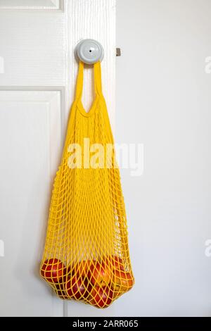 Nectarines in yellow string mesh reusable bag on the white door handle Stock Photo