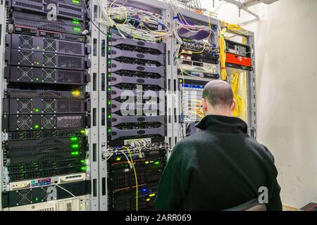 A man is sitting on a chair in the server room of the data center. The technician works with computer equipment. The system administrator configures s Stock Photo