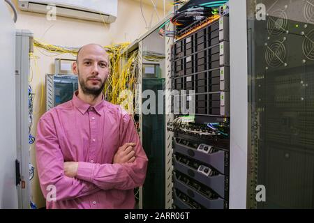 The man in the shirt is in the server room. The engineer stands on the background of servers and wires of the computer center. The young manager is in Stock Photo