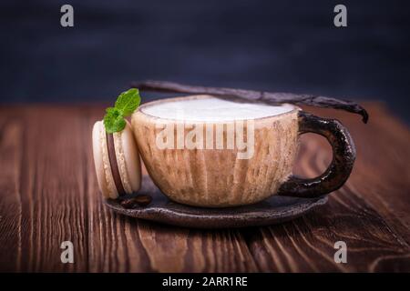 Coffee cappuccino, vanilla bean and chocolate macaroon or macaron with mint leaf on dark wooden background Stock Photo