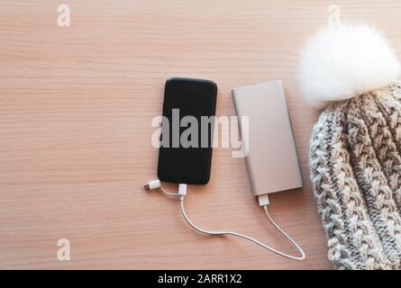 Mobile phone in winter charging from silver power bank, battery charger, on red toned background. Color image, high angle view. Portable charging devi Stock Photo