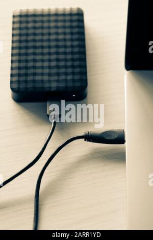 Black external hard disk, hdd connected with mini usb cable to laptop, green colored backgrpound. Modern technology concept. Stock Photo
