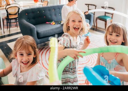 Three little sisters indoor at home playing with balloon having fun smiling - happiness, having fun, family concept Stock Photo