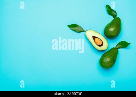 Fresh ripe organic green avocados and halve on color blue background, top view summer food concept. Minimal flat lay avocados whole fruit and halve on Stock Photo