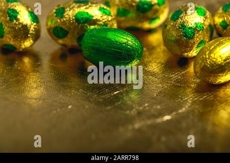 Chocolate easter eggs wrapped in yellow gold and green colored foil on golden background. Stock Photo