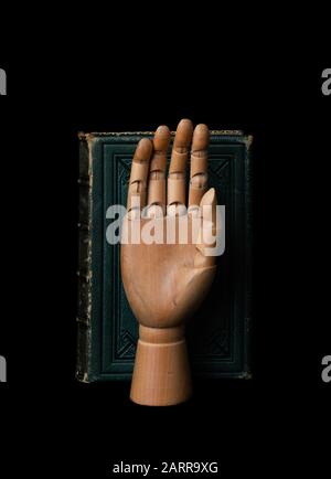 Wooden hand in front of old green leather bound book Stock Photo