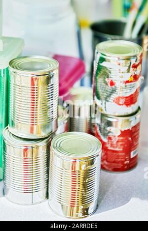 Close-up of damaged and peeled tin cans containing condensed milk, used in mixing milk shake, placed on a table next to kitchen utensils Stock Photo