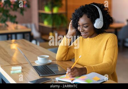 Smiling african girl in headphones looking at laptop, cafe interior Stock Photo