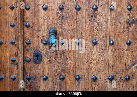 Ancient wooden door with nails, keyhole and hand-shaped knocker, he town of Margalef in winter, Lleida, Catalunya, Spain Stock Photo