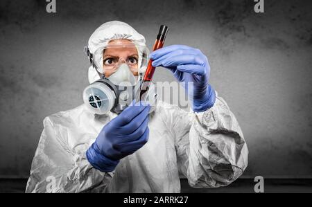 Woman In Hazmat Suit and Gas Mask Holding Test Tube of Blood In Dark Room. Stock Photo