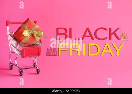 Small shopping cart with gift box and inscription BLACK FRIDAY on color background Stock Photo
