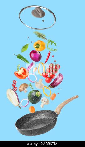 Frying pan and flying vegetables on color background Stock Photo