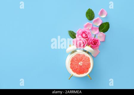 Beautiful rose flowers with alarm clock and ripe grapefruit on color background Stock Photo